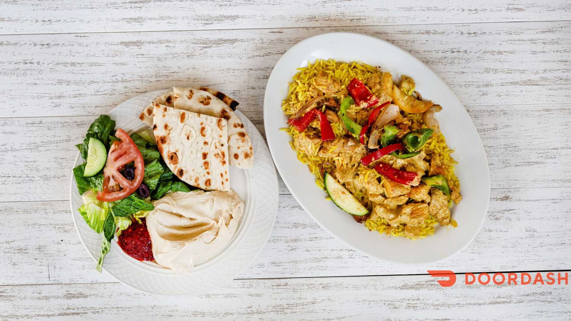 Chicken biryani with salad, flatbread, hummus on a white table. DoorDash logo in the corner.