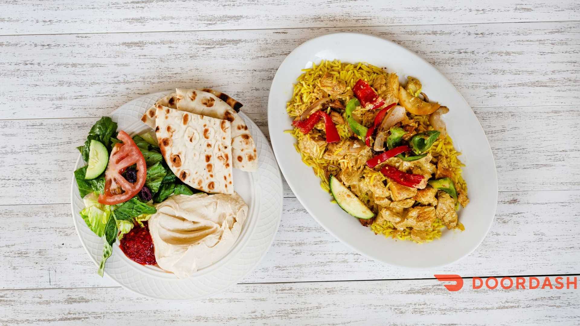 Chicken biryani with salad, flatbread, hummus on a white table. DoorDash logo in the corner.