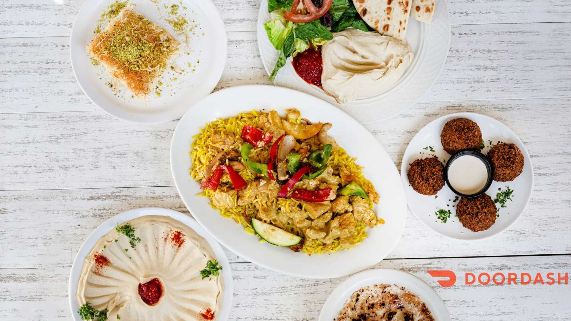 Middle Eastern dishes with rice, hummus, falafel, salad, and dessert on a white table.
